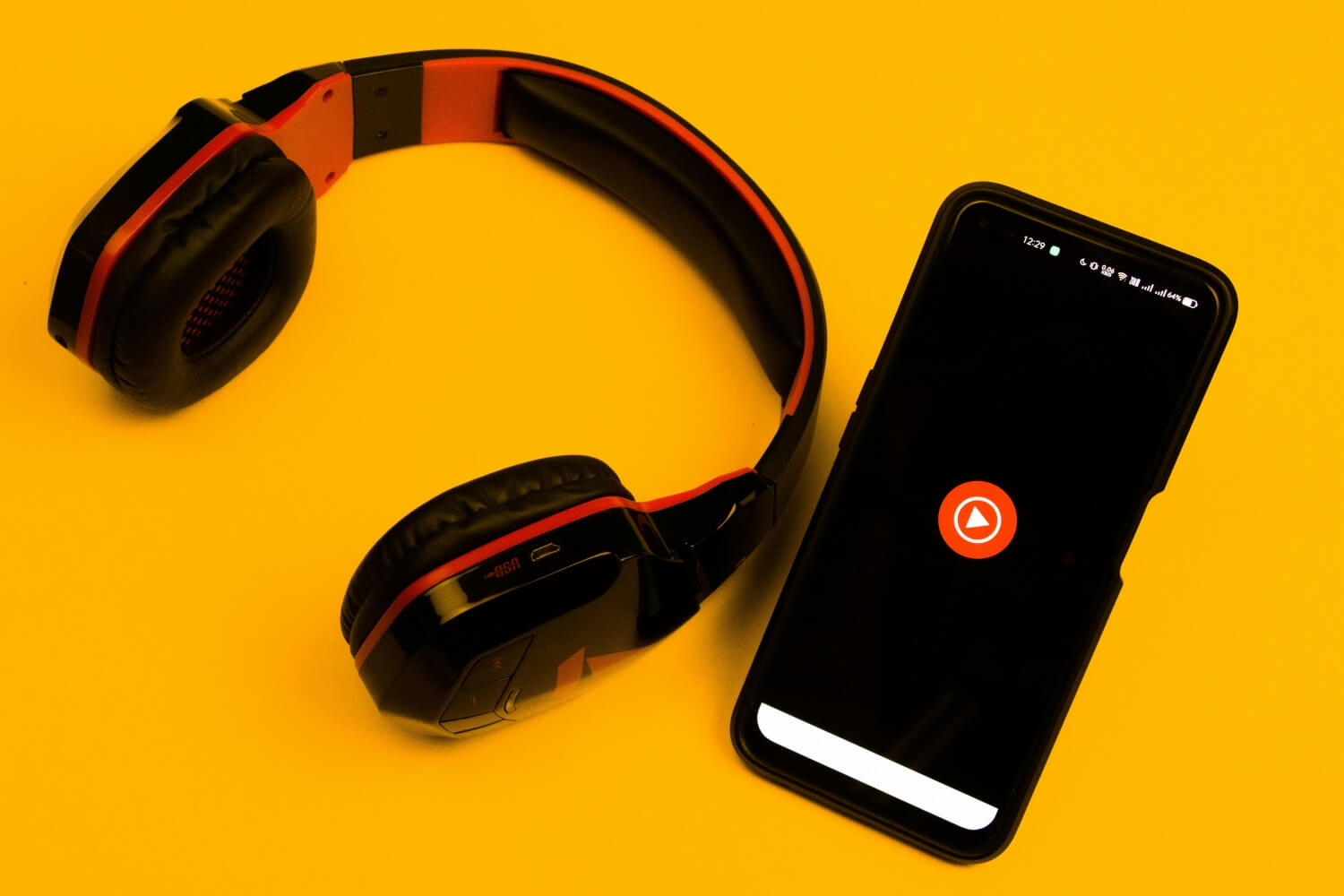 Słuchawki i telefon leżące na stole z włączonym audiobookiem. 